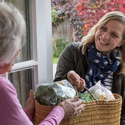 Elderly woman receiving a bag of groceries at her door.