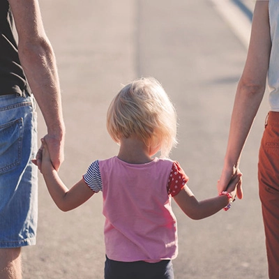 A child as seen from behind with a parent in each hand.