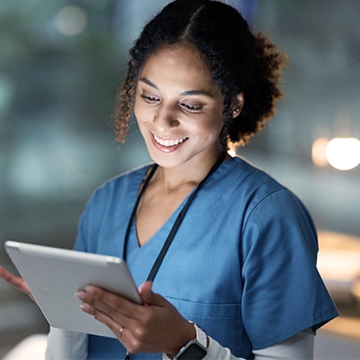 Woman in blue scrubs with a stethoscope around her neck and looking at a medical chart.