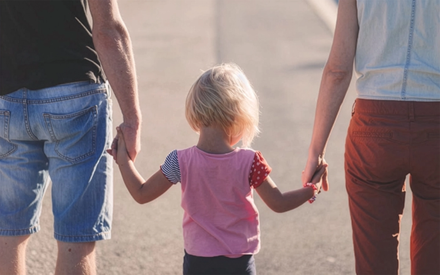 Rear view of a young child holding hands with a parent on either side.